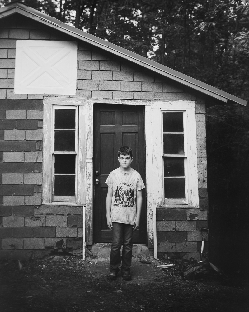 Black and white photograph of young boy in front of shed