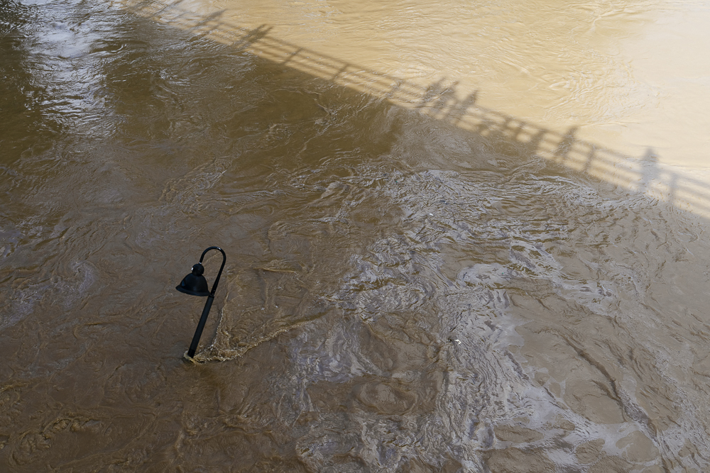Photograph of shadows of people on Haywood bridge looking down into floodwaters in River Arts District