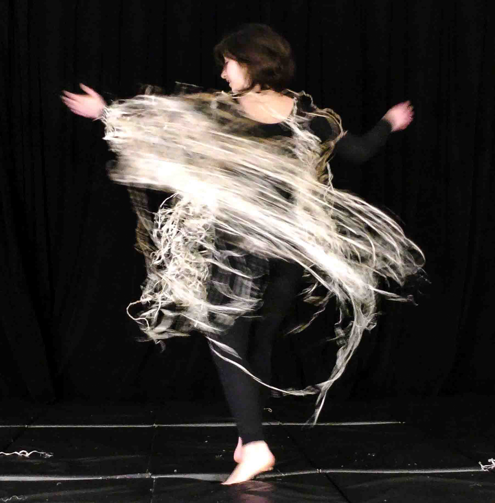 Person dancing with cape made out of kudzu fiber in dark room